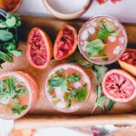 Blood Orange Kombucha Mojito on wooden tray with wooden muddler and mint leaves in a bowl of water