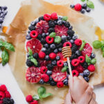 Berry Orange Fruit Pie on parchment paper with fresh basil and honey stick