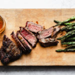 grilled steak cut into strips on a wooden bard with whiskey glass and asparagus on the side