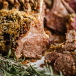 panko crusted lamb rack in a plate with rosemary on the side